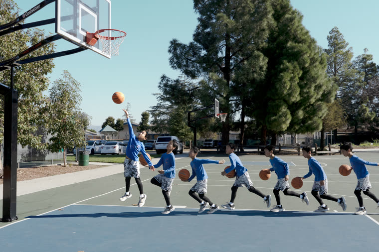 Children playing basketball on an outdoor court, a ball mid-air
