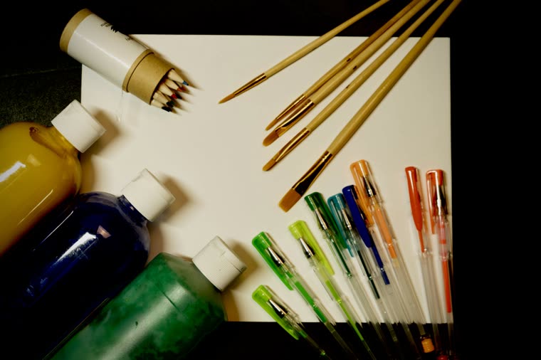 An overhead arrangement of paintbrushes, pens and markers