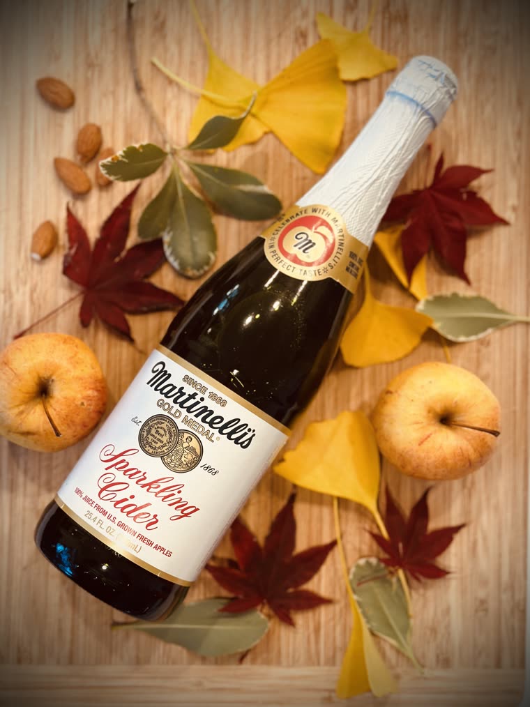 A bottle of sparkling cider styled with autumn leaves and apples