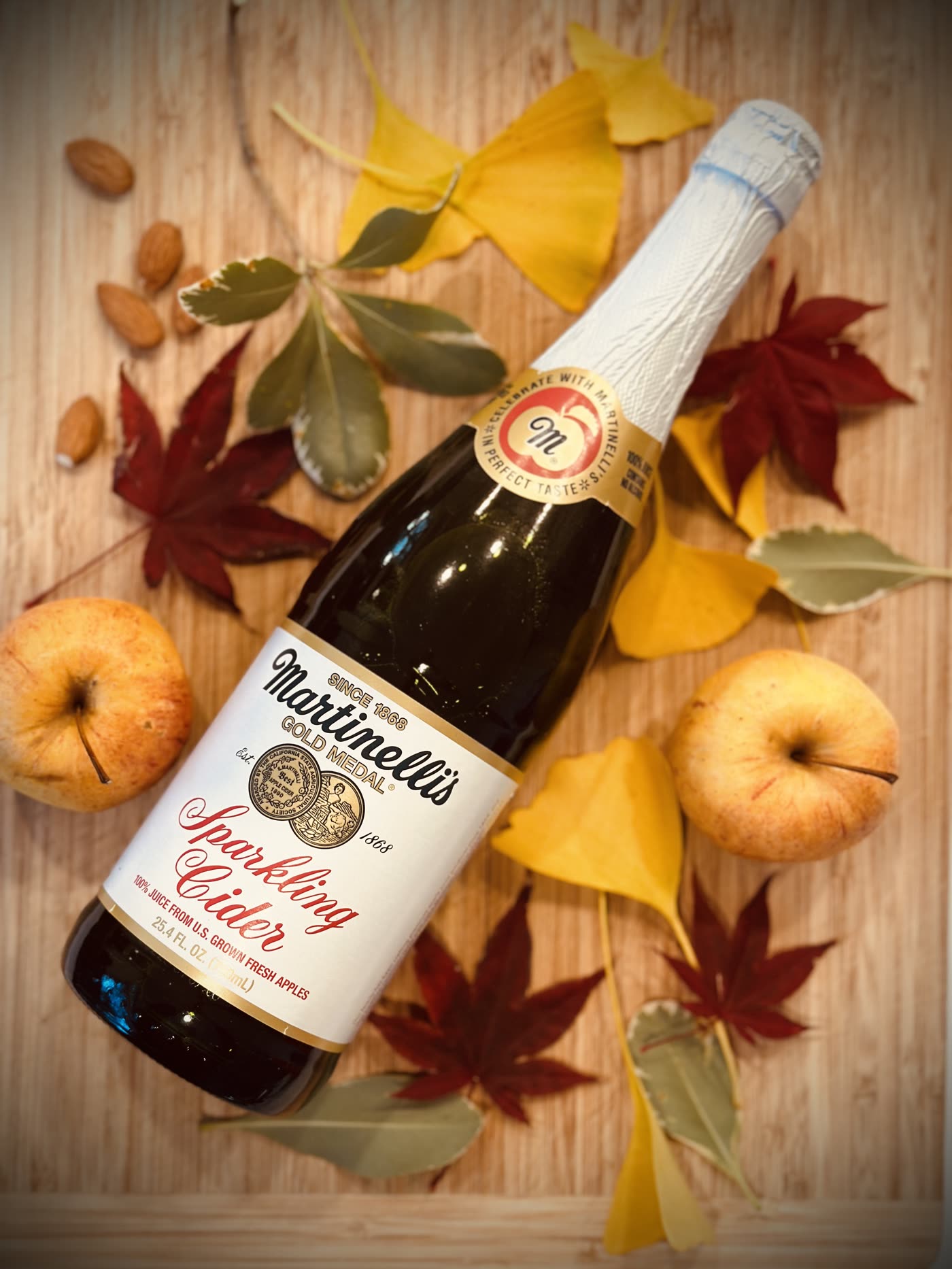 A bottle of sparkling cider styled with autumn leaves and apples
