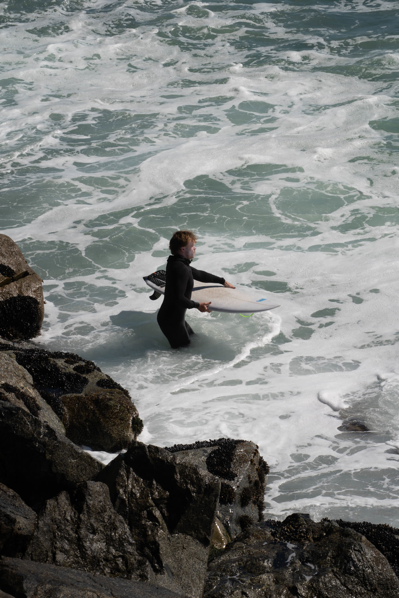 A surfer carrying a board into breaking waves