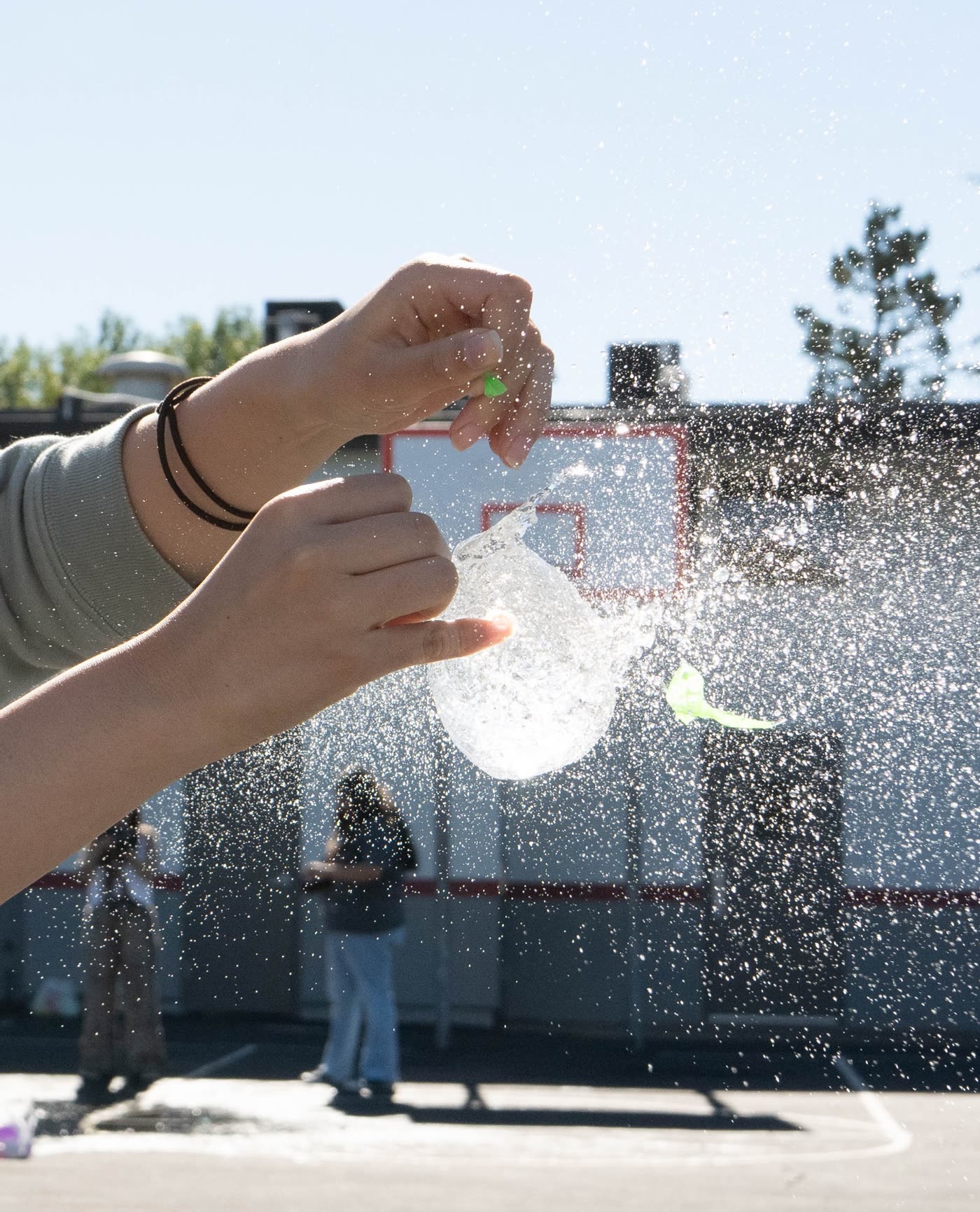 A water balloon bursting into backlit spray in someone's hands