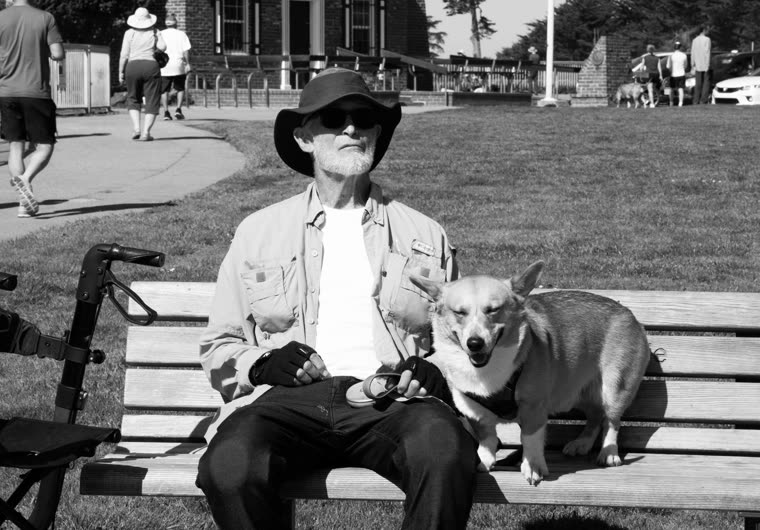 Black and white portrait of an older man sitting on a bench with his dog