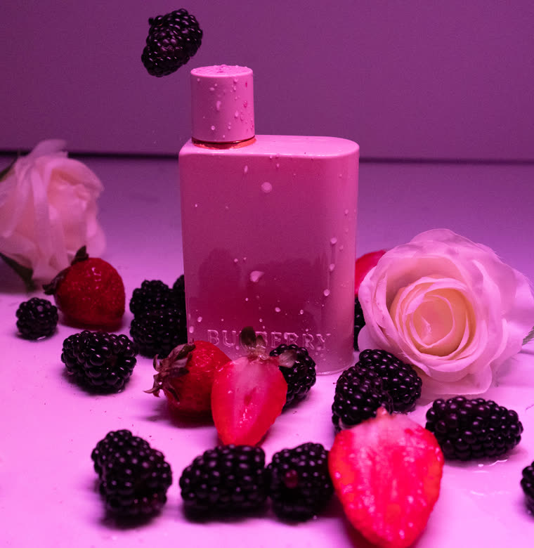 A pink perfume bottle styled with blackberries, strawberries and roses