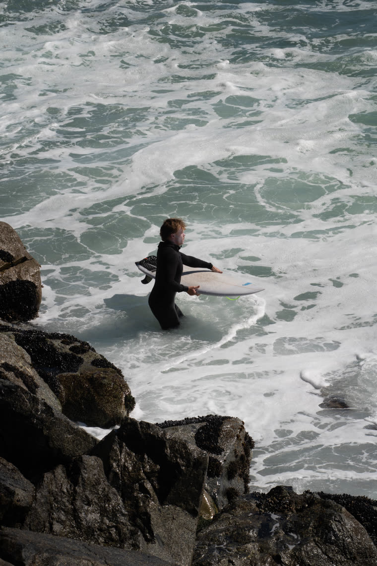 A surfer carrying a board into breaking waves
